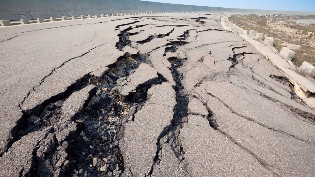 Close-up of a road severely cracked and damaged with deep fissures running through the asphalt.