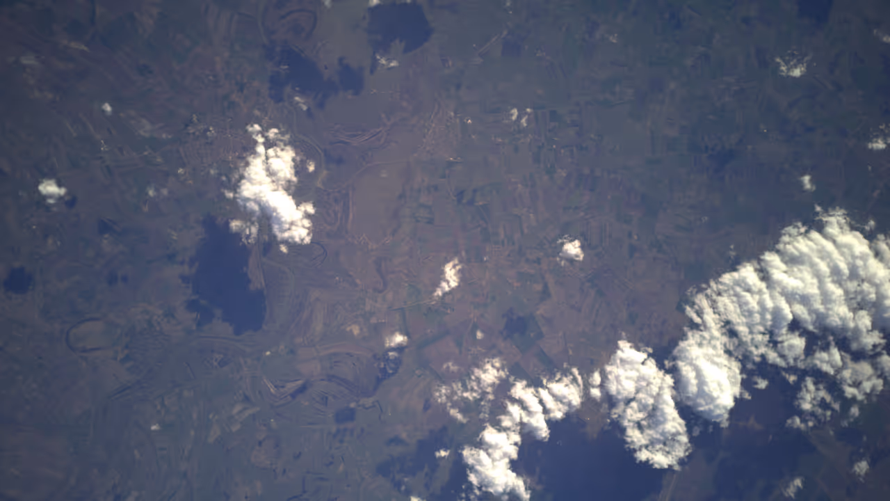 Aerial view of rural landscape with patchwork fields and scattered clouds casting shadows.